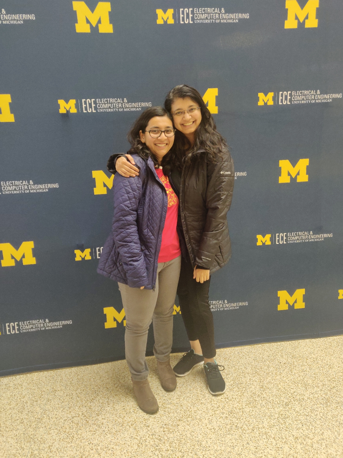 two women stand in front of a backdrop of Michigan ECE logos